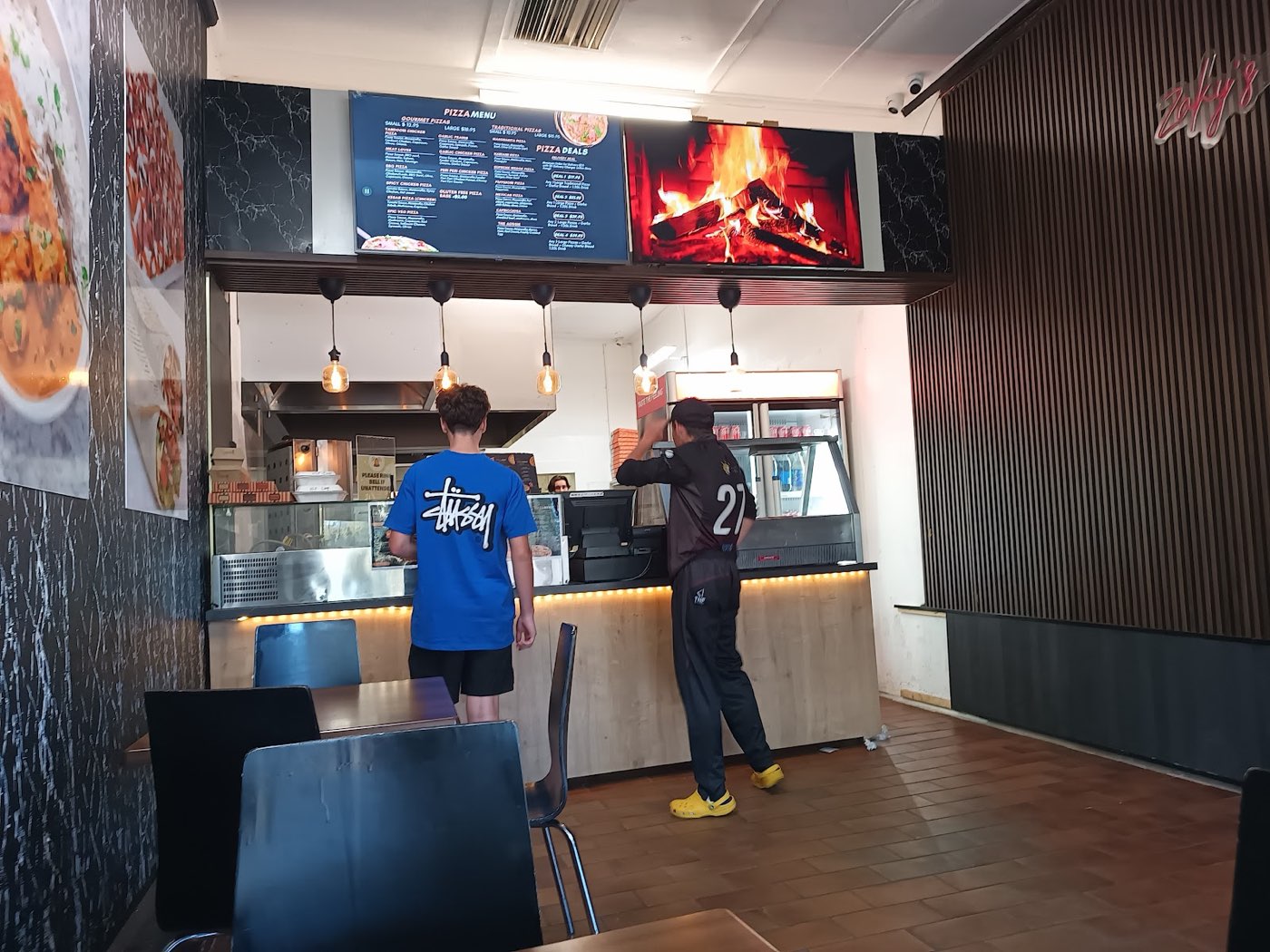Inside the shop: the ordering counter under menu screens, with a dark panelled wall, black chairs and a tiled floor
