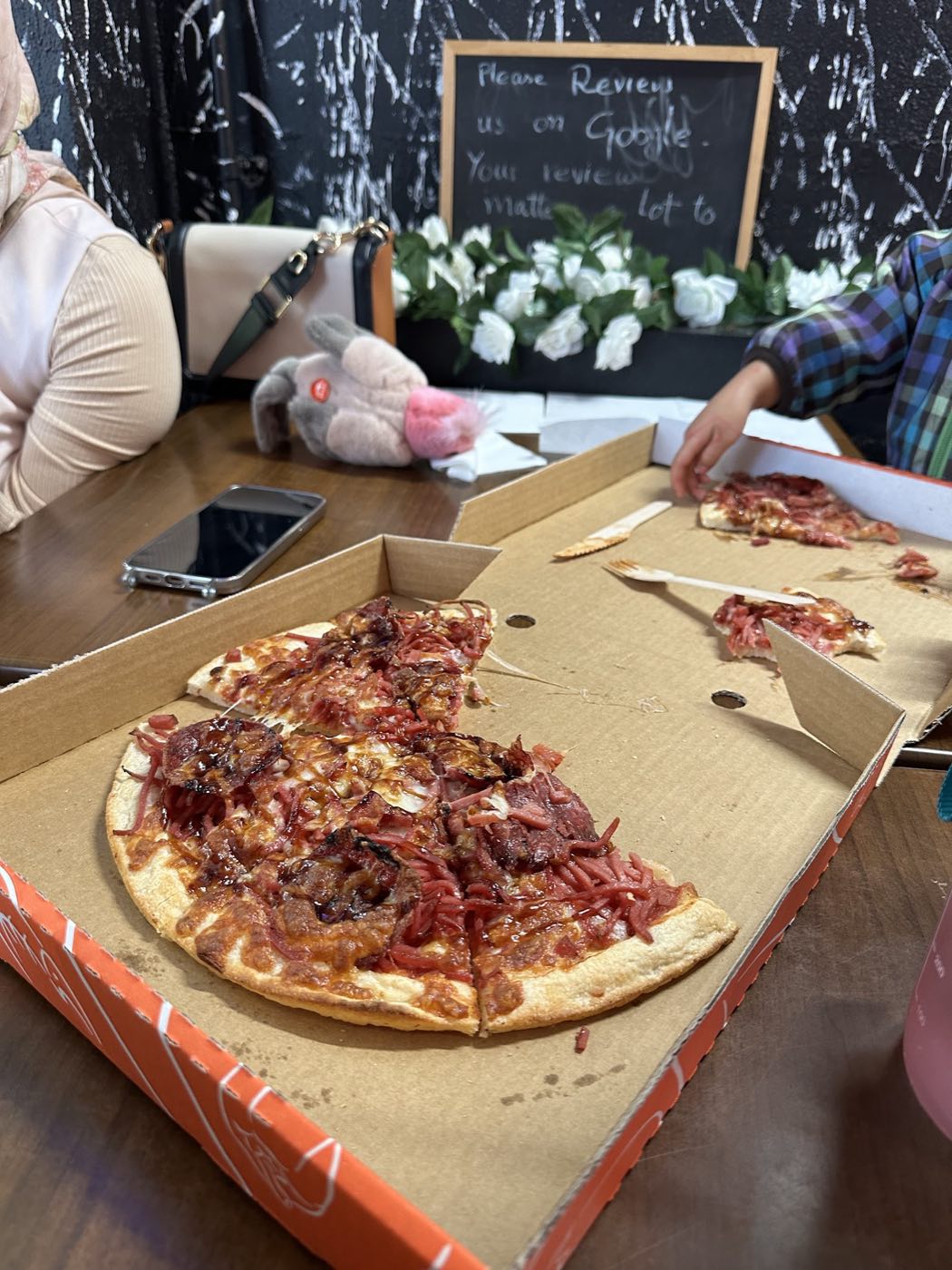 A large pizza with a dark, saucy meat topping, partly eaten, in an orange box on a table